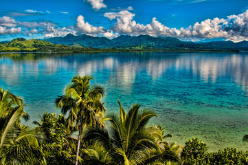 Lush tropical landscape with turquoise waters and distant mountains under a blue sky.